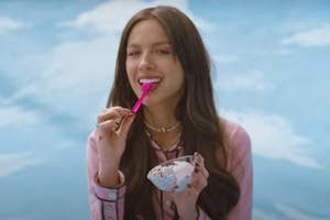 Olivia Rodrigo eating ice cream with a spoon and a sky background.