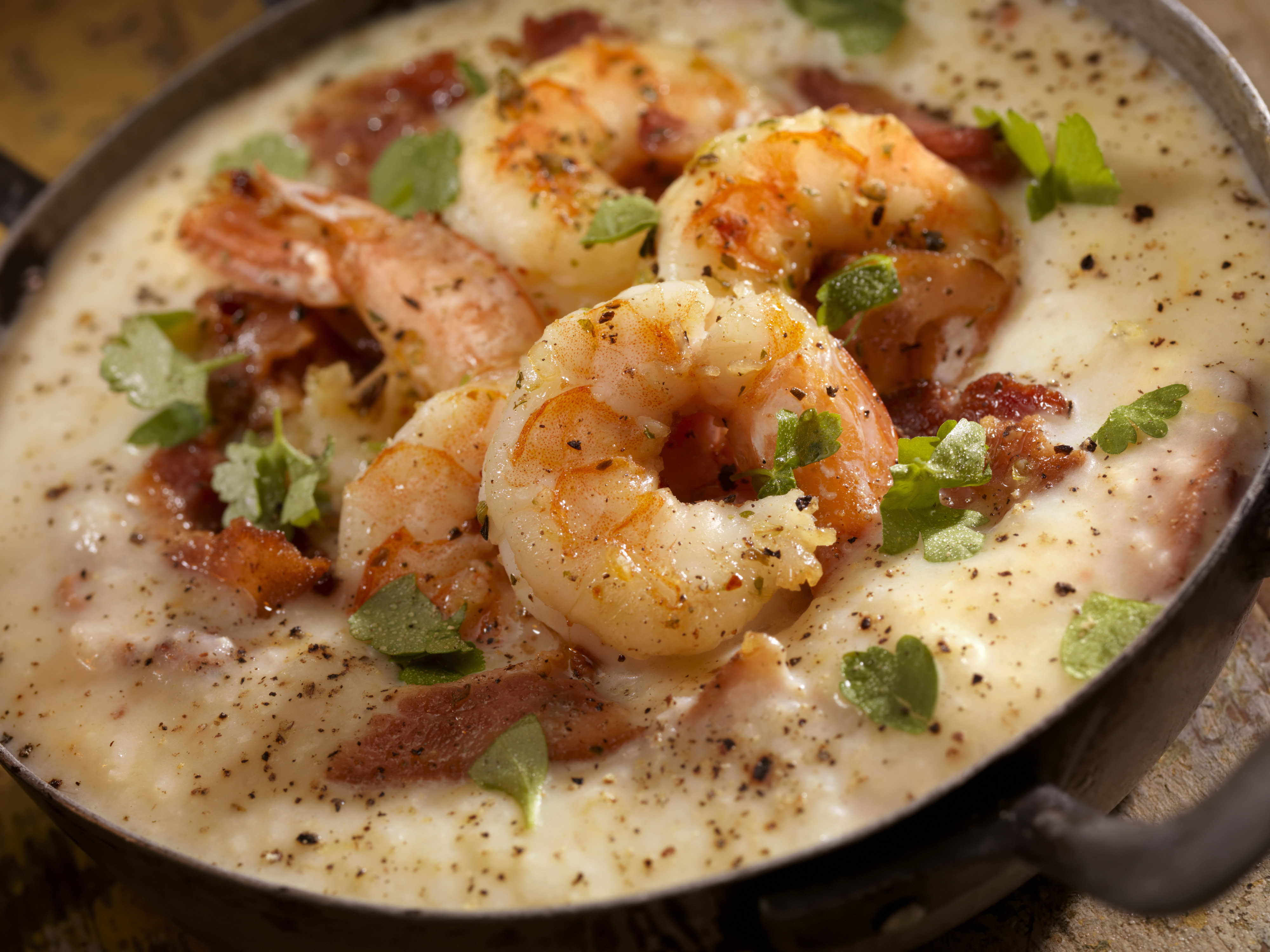 A close-up of a shrimp and grits dish, featuring plump shrimp, crispy bacon bits, and garnished with fresh herbs
