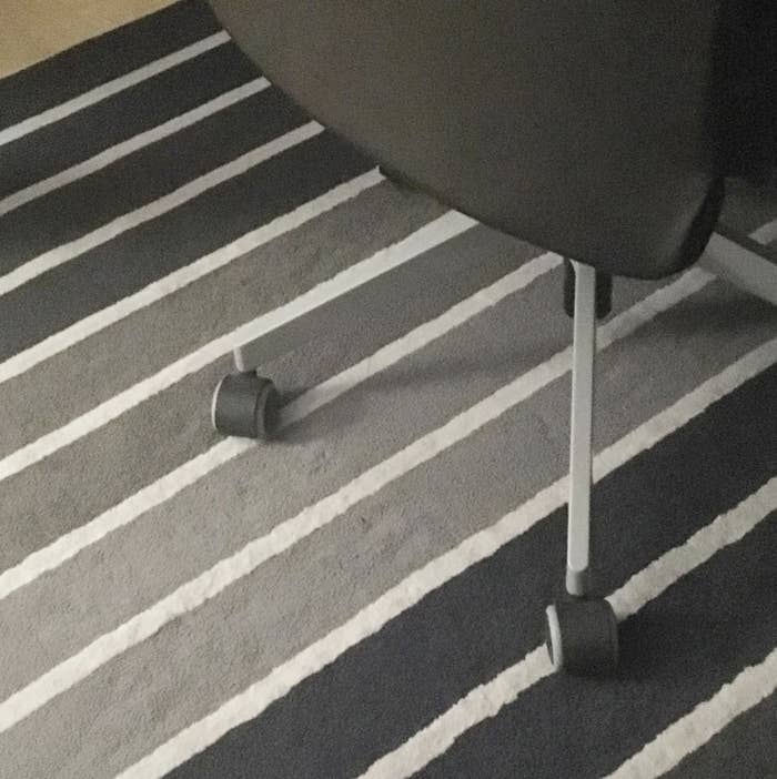 A close-up shot of the legs and wheels of a rolling office chair on a striped rug