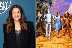 Drew Barrymore in a black blazer next to a poster of The Wizard of Oz with Dorothy, Scarecrow, Tin Man, and Cowardly Lion on the yellow brick road