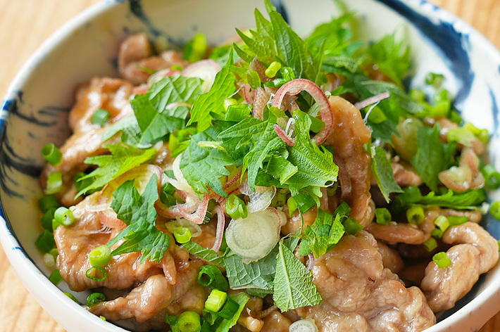白いボウルに盛られた肉と薬味がのった料理。