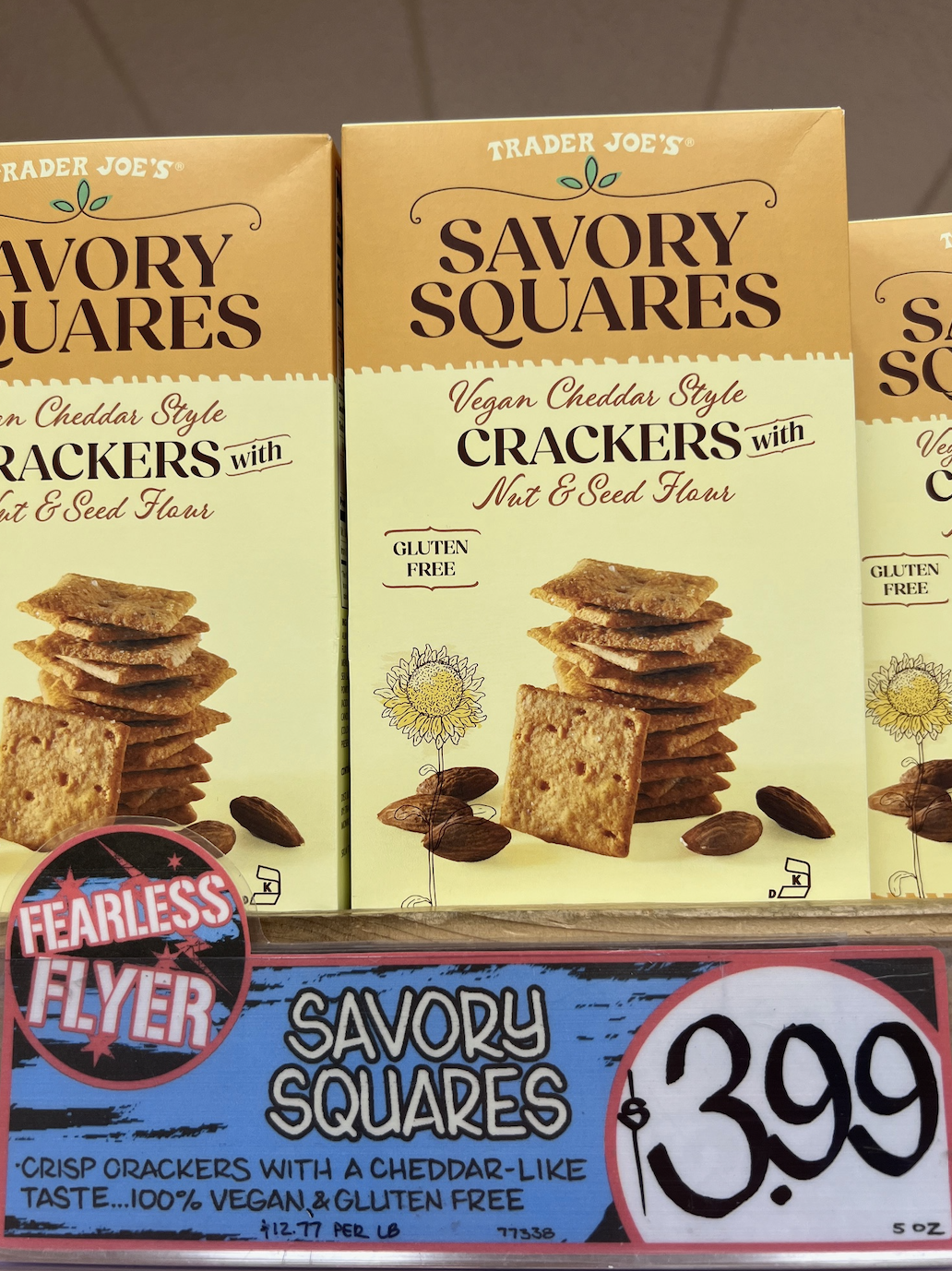 Boxes of Trader Joe's Savory Squares Vegan Cheddar Style Crackers with Nut & Seed Flour are displayed, labeled gluten-free and priced at $3.99