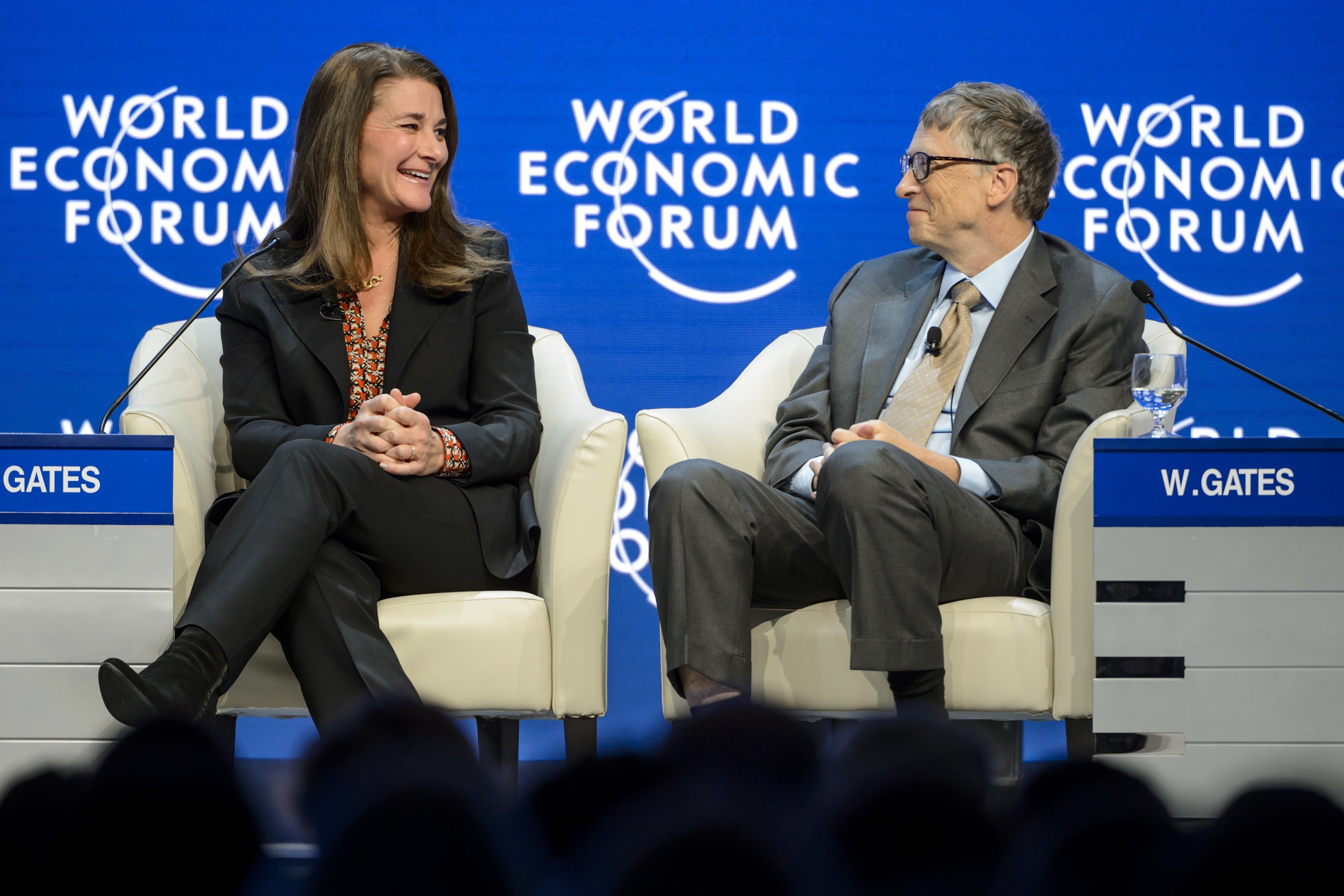 Melinda Gates and Bill Gates seated and smiling at the World Economic Forum, both dressed in formal business attire
