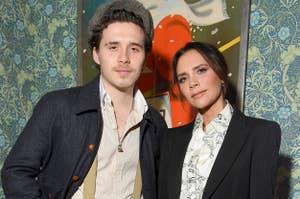 Brooklyn Beckham and Victoria Beckham pose together at an event, with both wearing stylish, semi-formal outfits