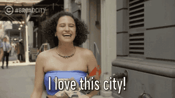 Ilana Glazer from Broad City laughing and holding a bag, with the text "I love this city!"