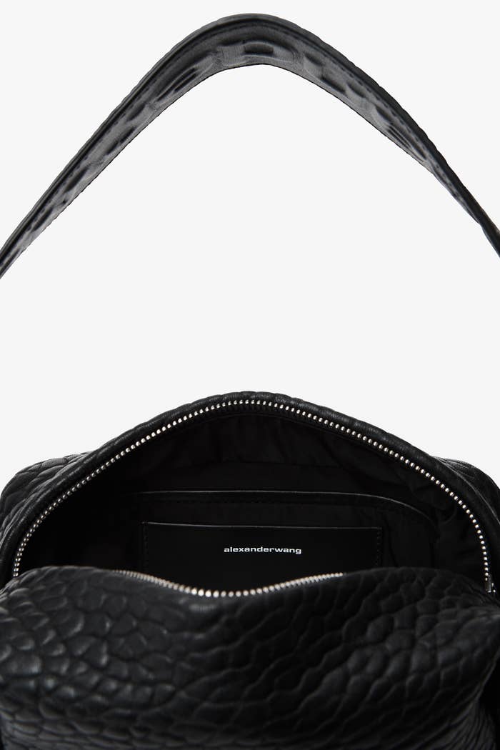 Close-up image of an open Alexander Wang handbag with a textured leather finish and visible interior zipper pocket. The Alexander Wang logo is seen inside