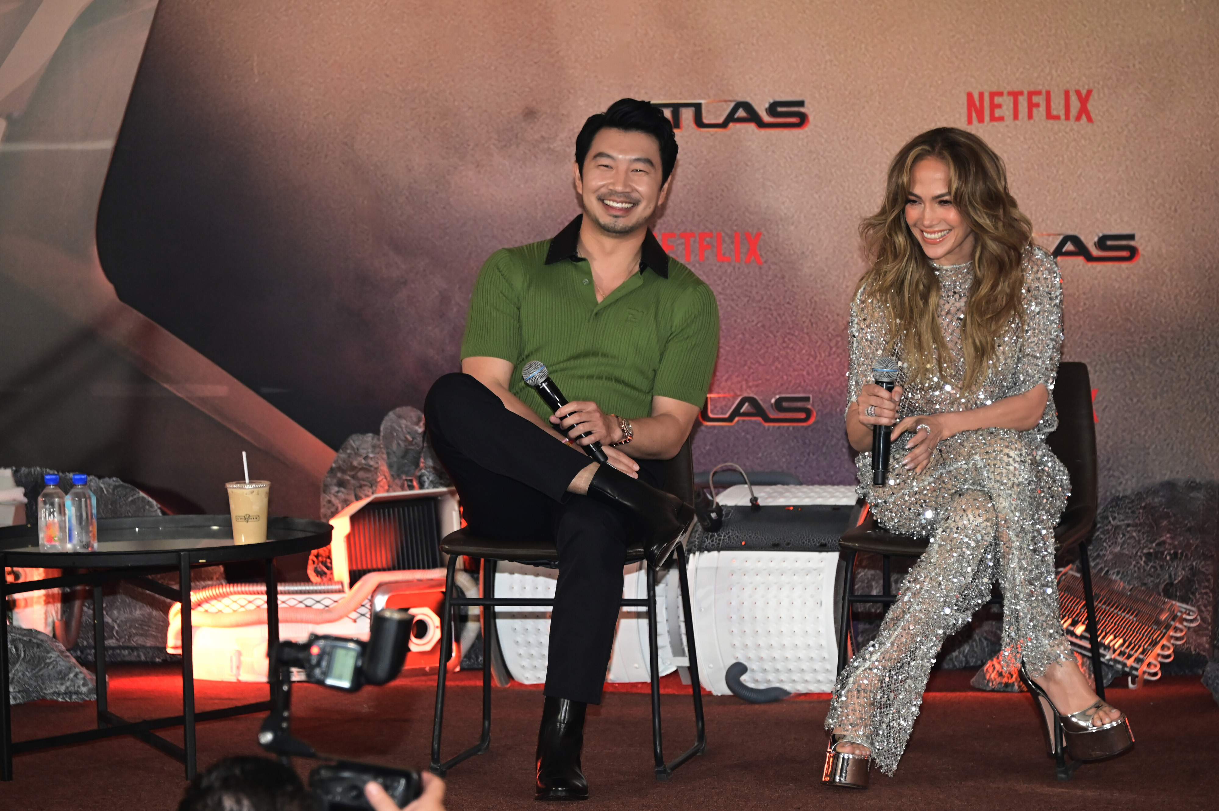 Simu Liu and Jennifer Lopez sit and smile during a Netflix event