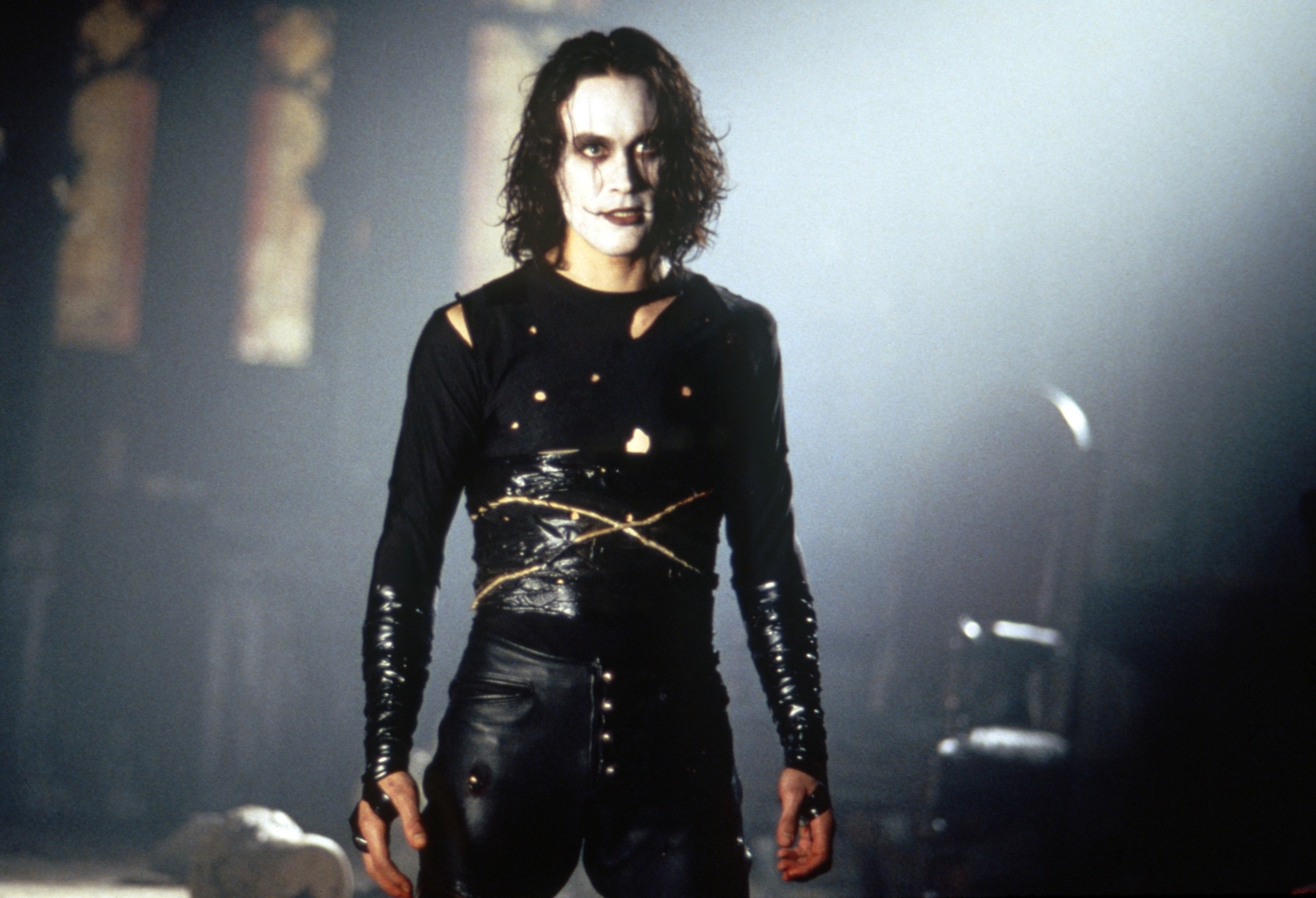 Vincent Perez in leather clothing with gothic makeup, in a dimly lit setting in a scene