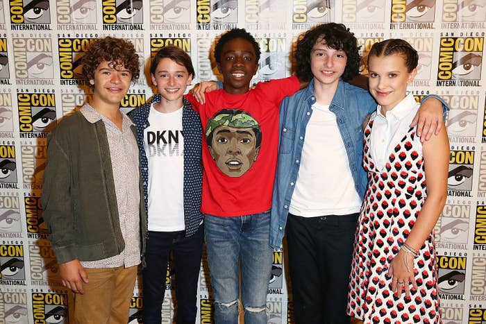 Gaten Matarazzo, Noah Schnapp, Caleb McLaughlin, Finn Wolfhard, and Millie Bobby Brown pose together at San Diego Comic-Con in front of an event backdrop