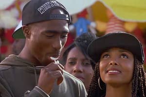 Tupac Shakur in a hoodie and cap, licking a lollipop. Janet Jackson beside him, wearing a cap and hoop earrings. They appear to be outdoors at an event