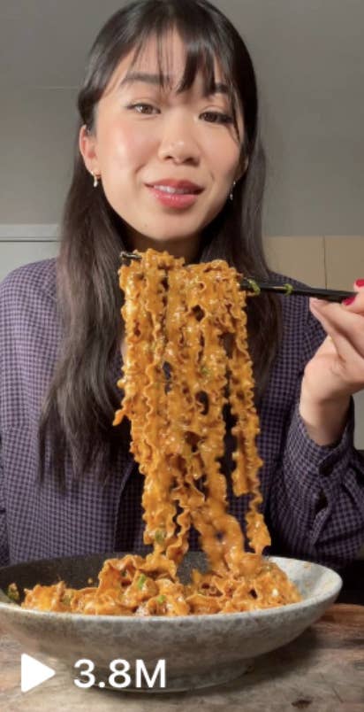 A woman with long hair and bangs holds up a forkful of noodles while smiling at the camera. The video has 3.8 million views