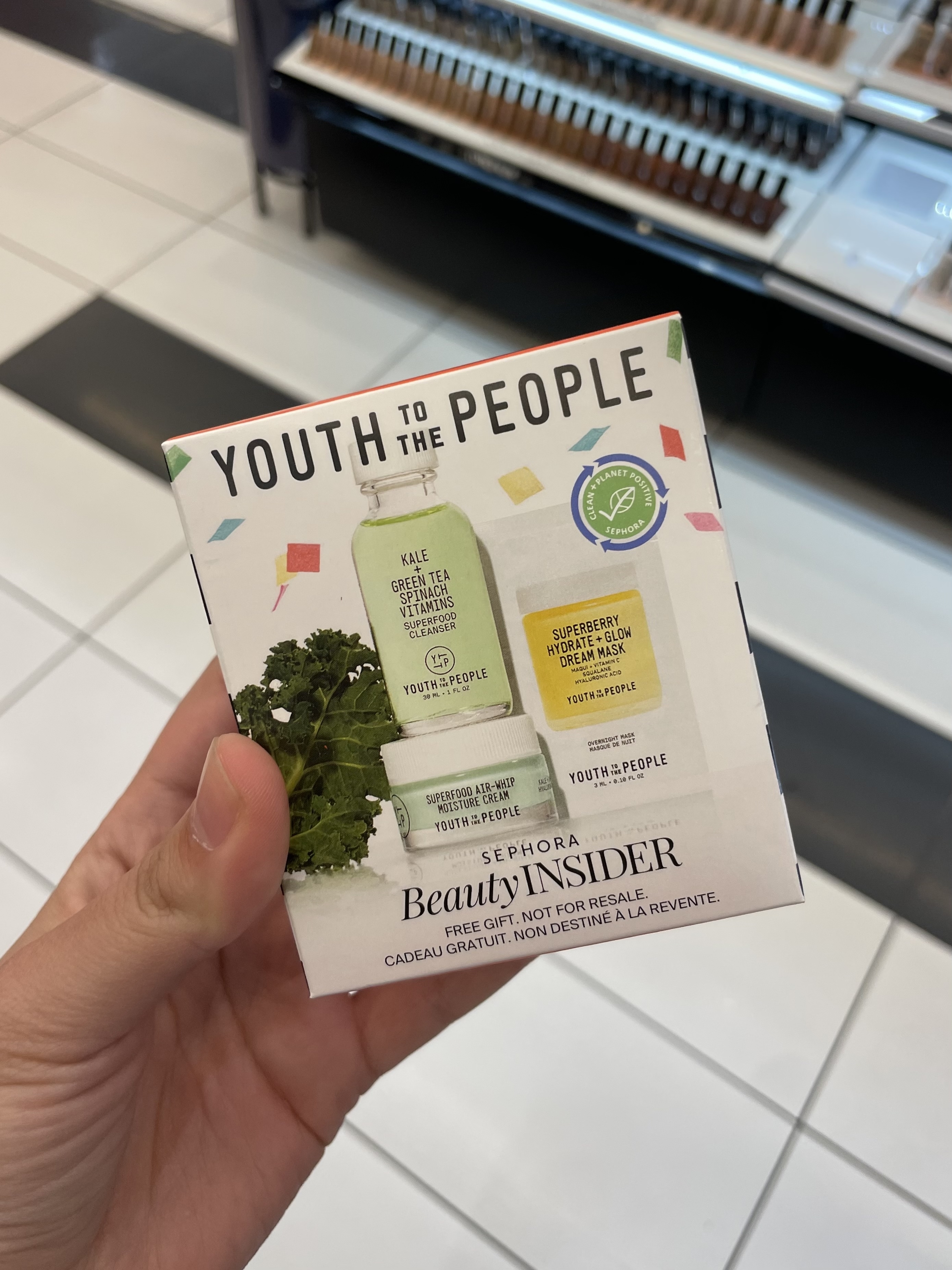Person holding Youth to the People skincare gift box, promoting superfood ingredients like kale and spinach, in a Sephora store