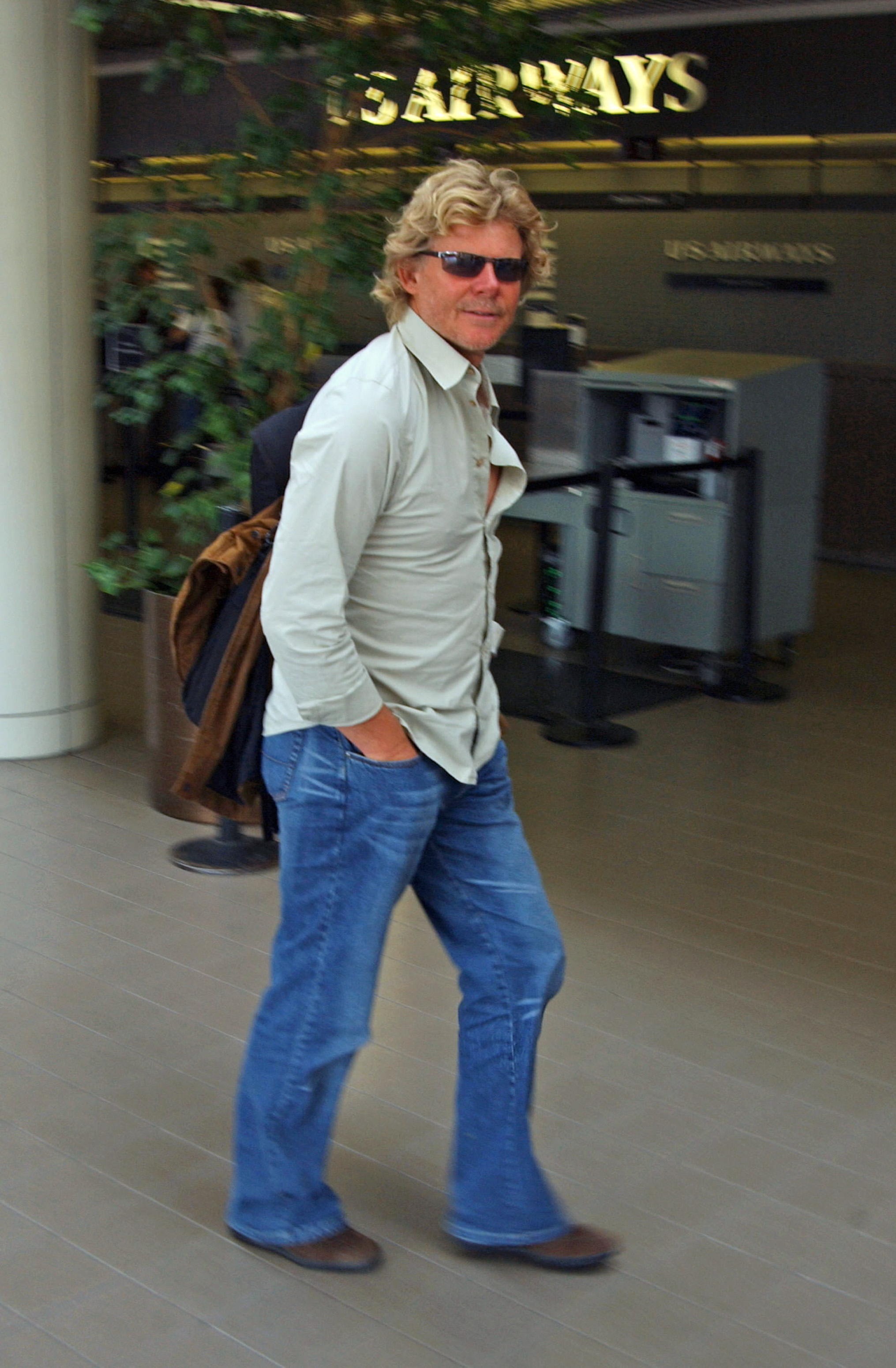 Mutt Lang, wearing sunglasses, a light-colored shirt, and jeans walking outside