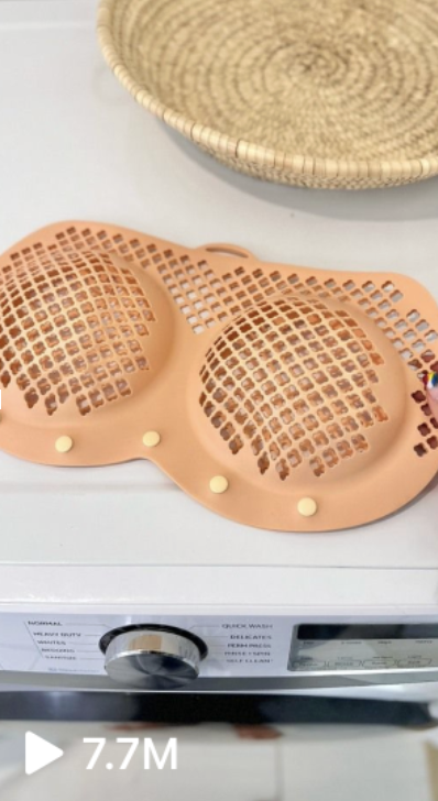 A bra with a ventilated design is laid flat on a washing machine's open door. A woven basket is in the background. The video has 7.7M views
