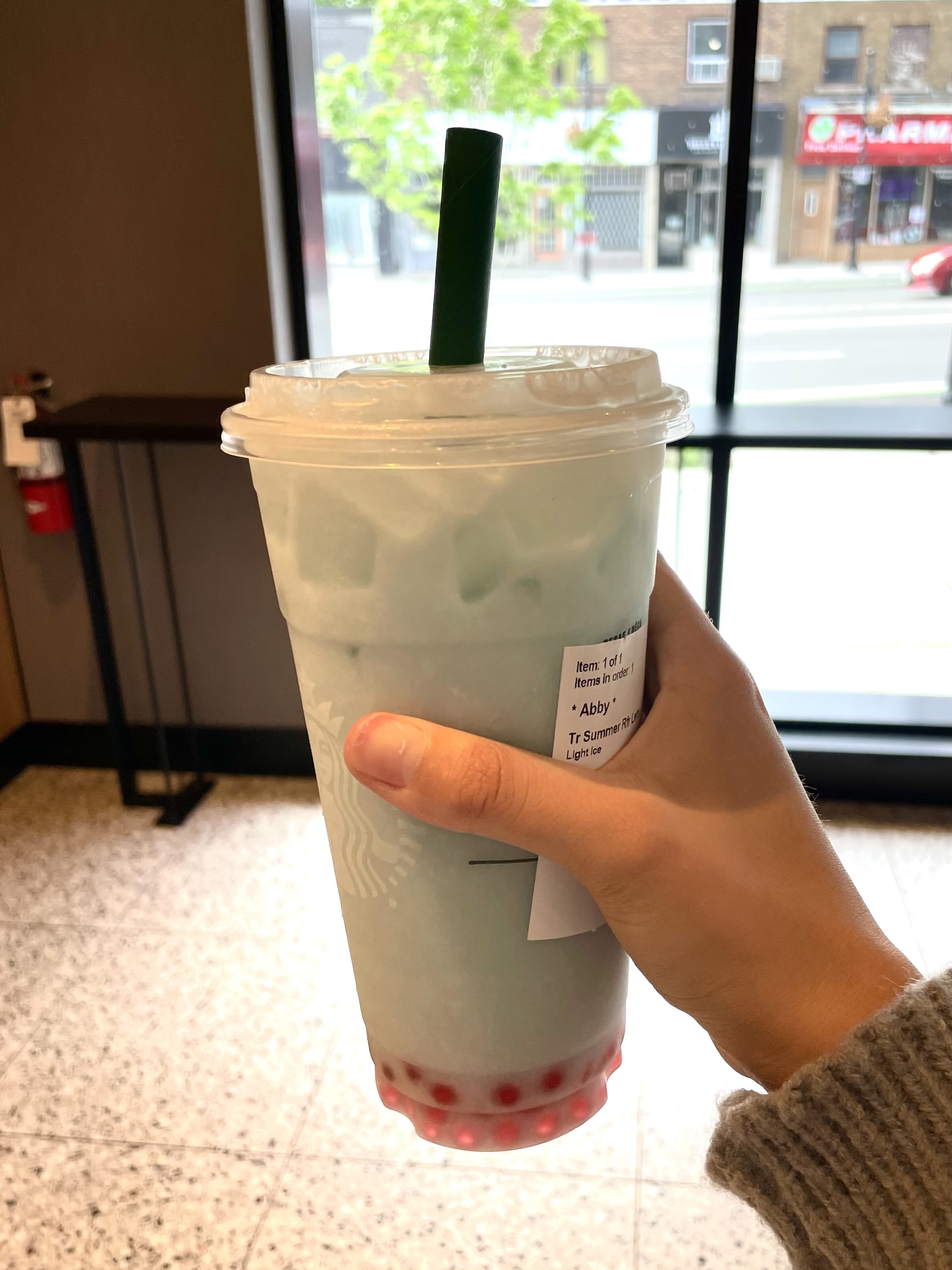 Close-up of a hand holding a bubble tea with tapioca pearls and a green straw in a cafe