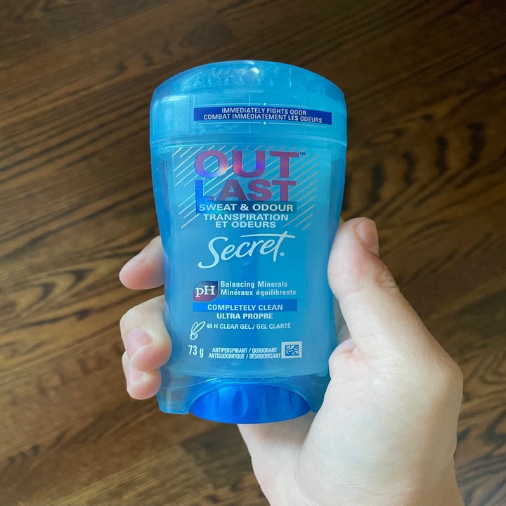 A hand is holding a Secret Outlast Sweat & Odour deodorant stick with a label highlighting balancing minerals and "completely clean" scent