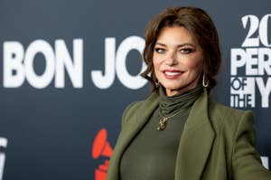 Shania Twain on a red carpet wearing an olive green turtleneck and matching blazer, smiling