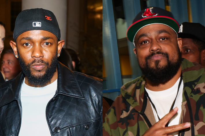 Kendrick Lamar in a black leather jacket and cap stands next to DJ Drama in a camo jacket and cap, both at an event