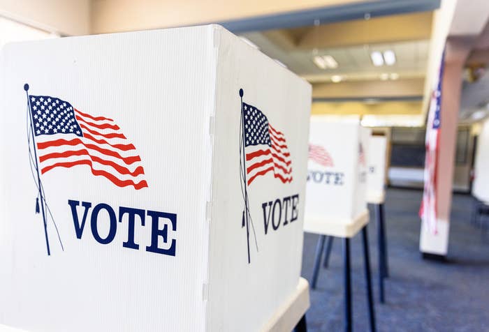 Voting booths lined up in a room, each displaying an American flag and the word "VOTE"