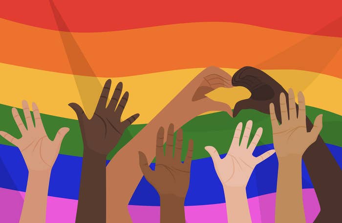 People of diverse skin tones raise their hands and form a heart shape in front of a rainbow pride flag