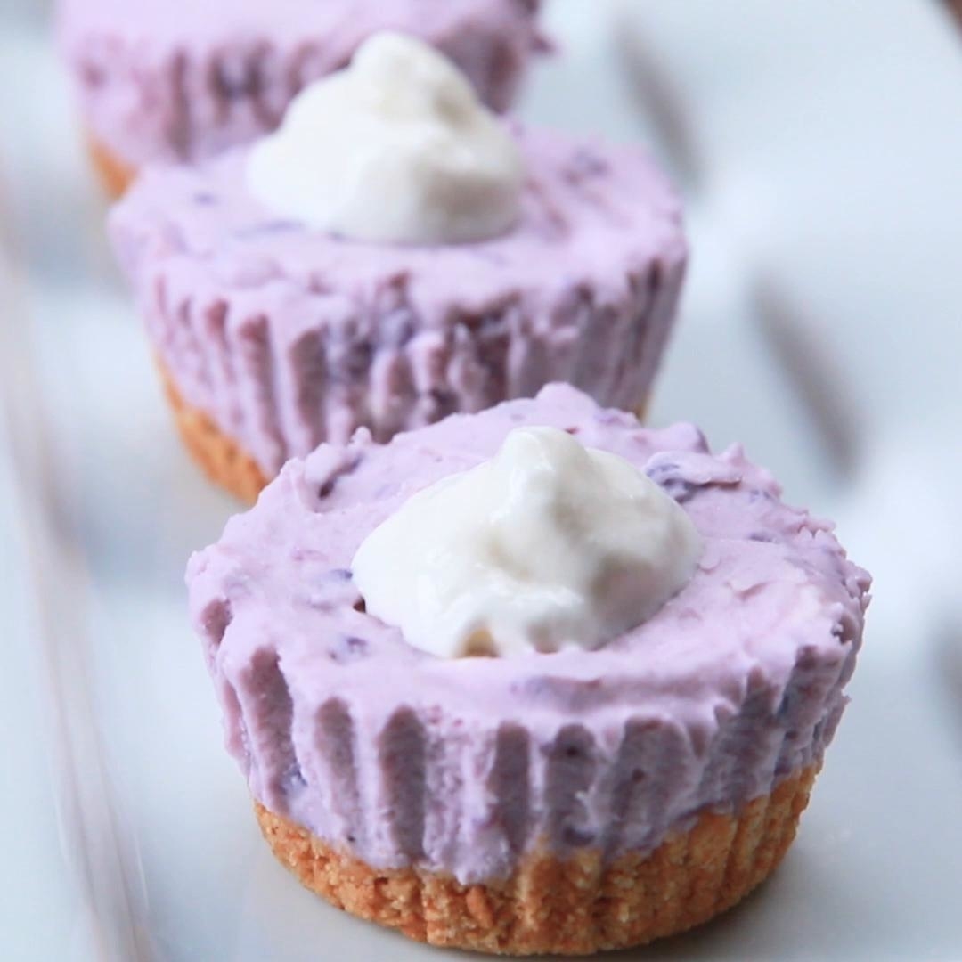 Three mini blueberry cheesecakes with whipped cream tops arranged in a row on a white surface