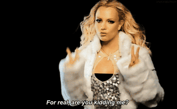 Britney Spears in a sparkly top and fur coat, gesturing with two fingers on each hand. Text overlay: "For real, are you kidding me?"