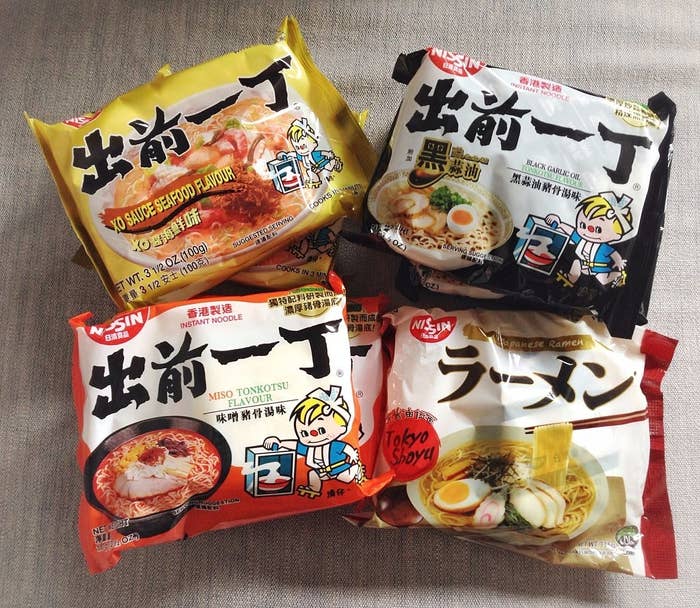 Four Nissin instant noodle packages in different flavors: Soy Sauce Seafood, Miso Tonkotsu, Black Garlic, and Tokyo Shoyu