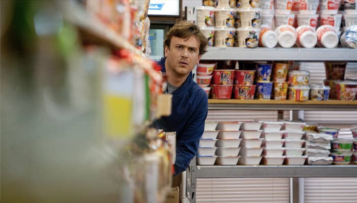 A man in a grocery store aisle, looking intently ahead, with shelves stocked with various packaged foods surrounding him