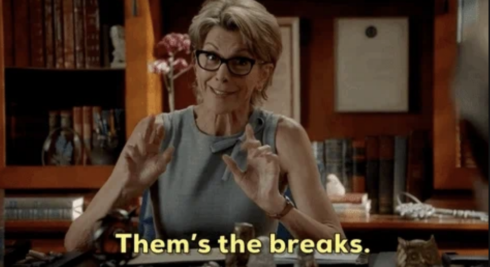 A dean is sitting at a desk filled with books and papers, wearing glasses and a sleeveless top. The text overlay reads, "Them's the breaks."