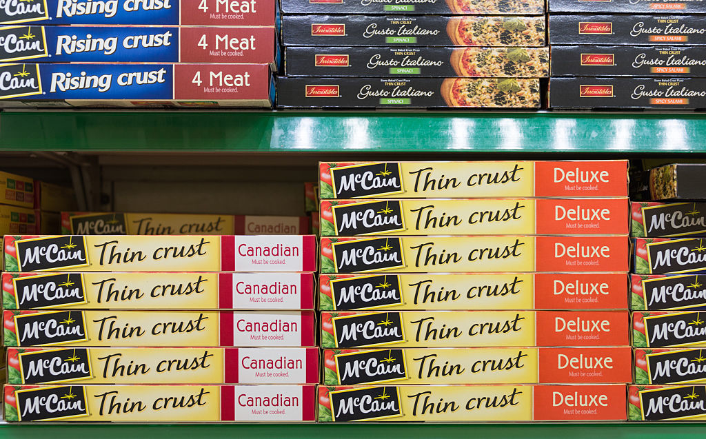 Frozen pizza boxes arranged on grocery store shelves, including McCain Thin Crust, McCain Rising Crust, and other pizza brands