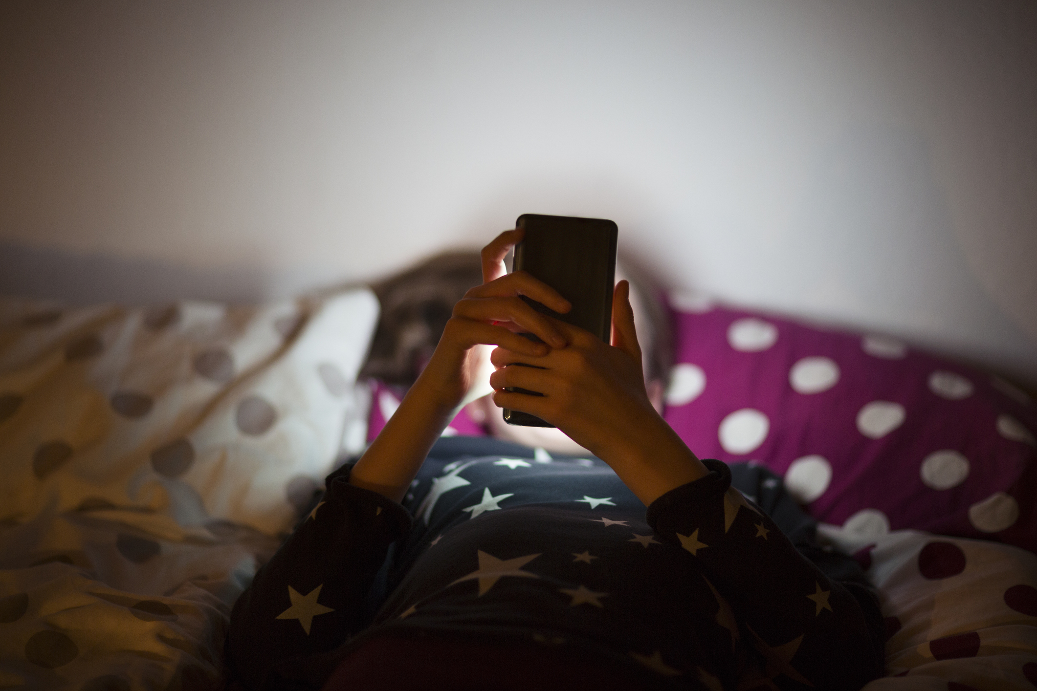 Person lying in bed using a smartphone, with patterned bedding around them