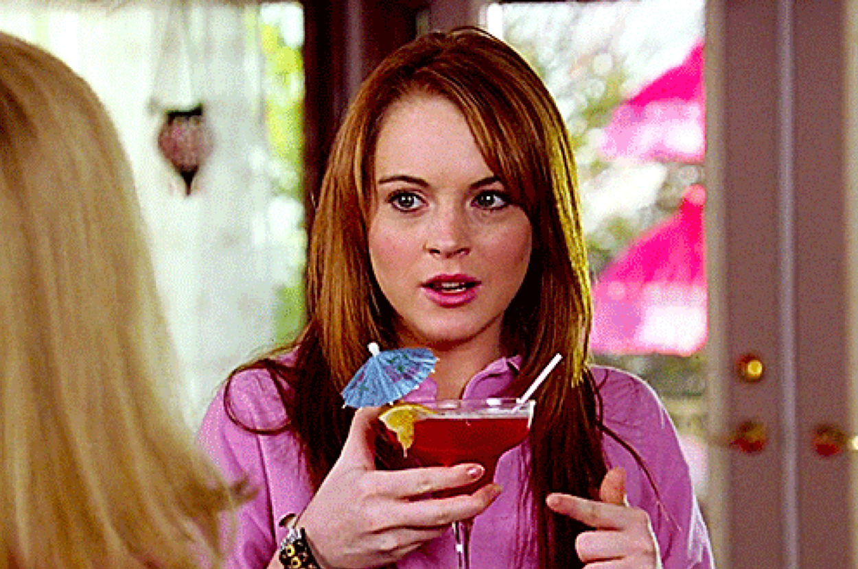 Lindsay Lohan holds a cocktail garnished with a lime wedge and an umbrella while talking to another person out of frame