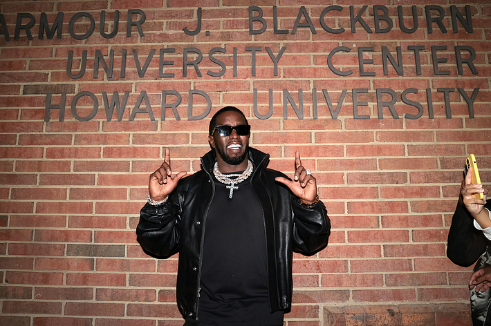 Sean "Diddy" Combs stands in front of the Armour J. Blackburn University Center at Howard University, smiling and pointing upwards