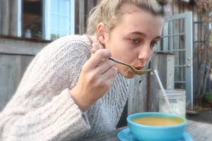 Emma Chamberlain sits at an outdoor table, sipping soup from a spoon