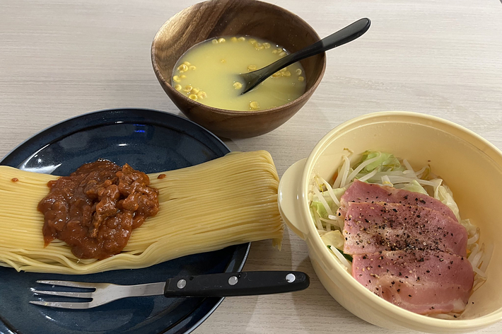 パスタとミートソース、スープ、ハムと野菜のサラダがテーブルに置かれています。