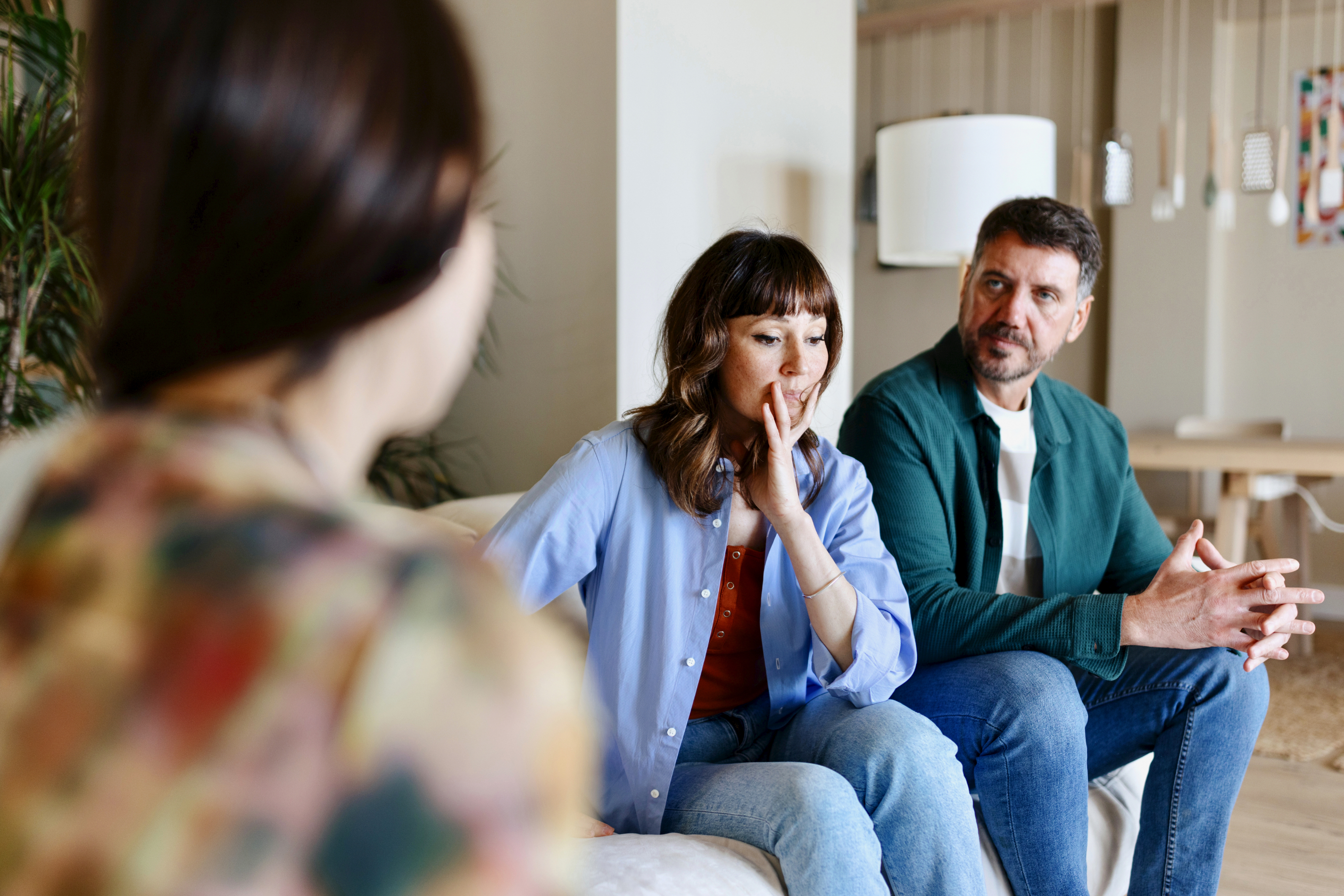 A person speaks to a worried-looking couple sitting on a couch