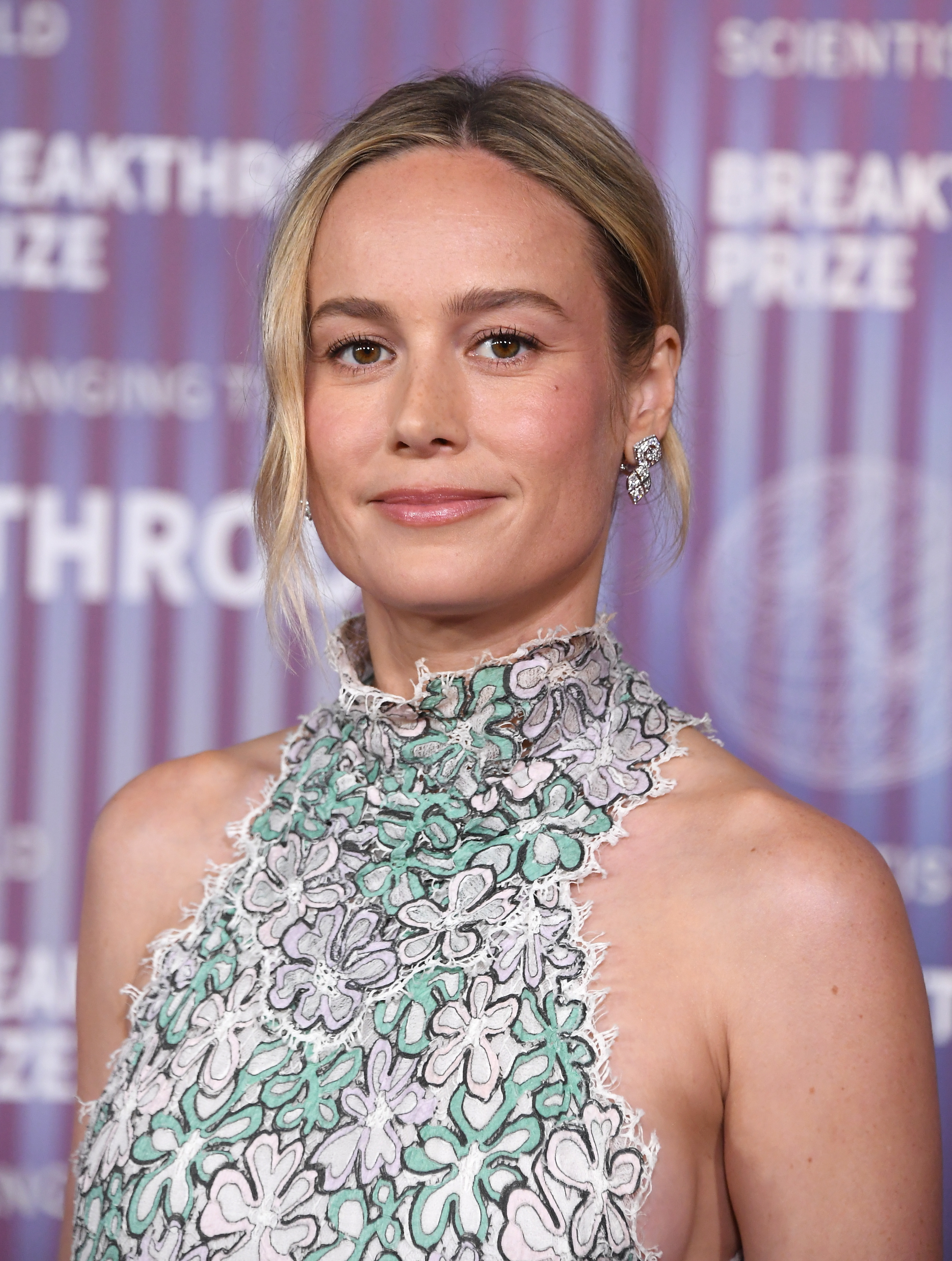 Brie Larson on the red carpet at the Breakthrough Prize event, wearing a high-neck lace dress with floral patterns
