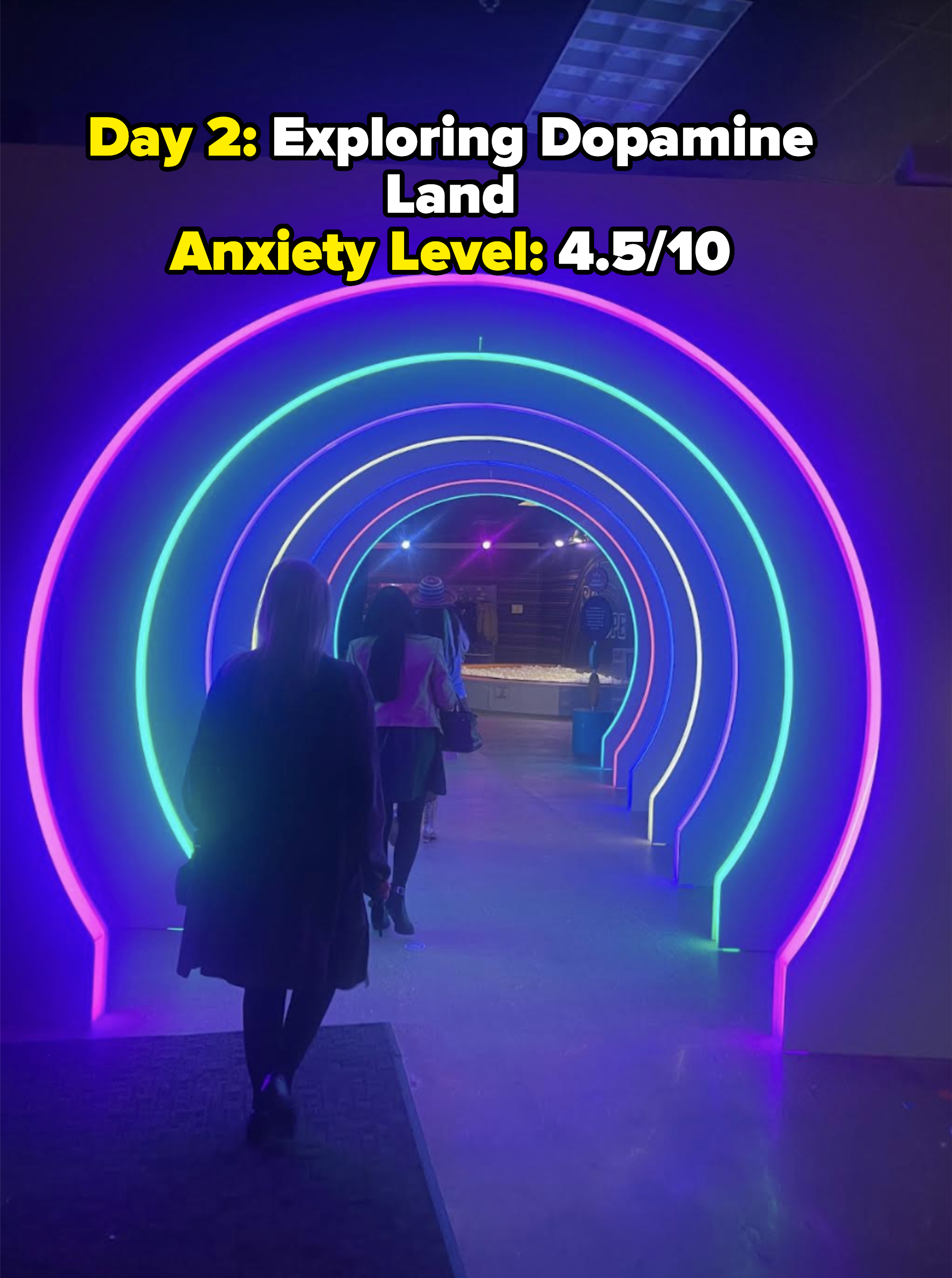 People walking through a neon-lit tunnel with concentric glowing arches at what appears to be a modern exhibit or event space