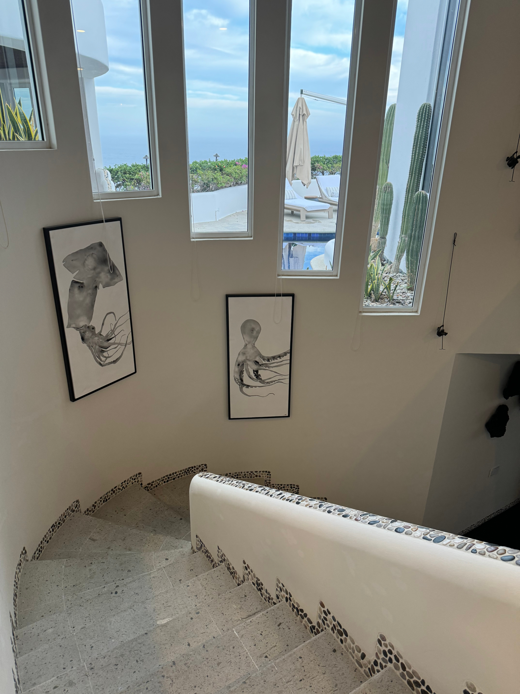 Spiral staircase with ocean view through tall windows, adorned with two framed octopus art pieces