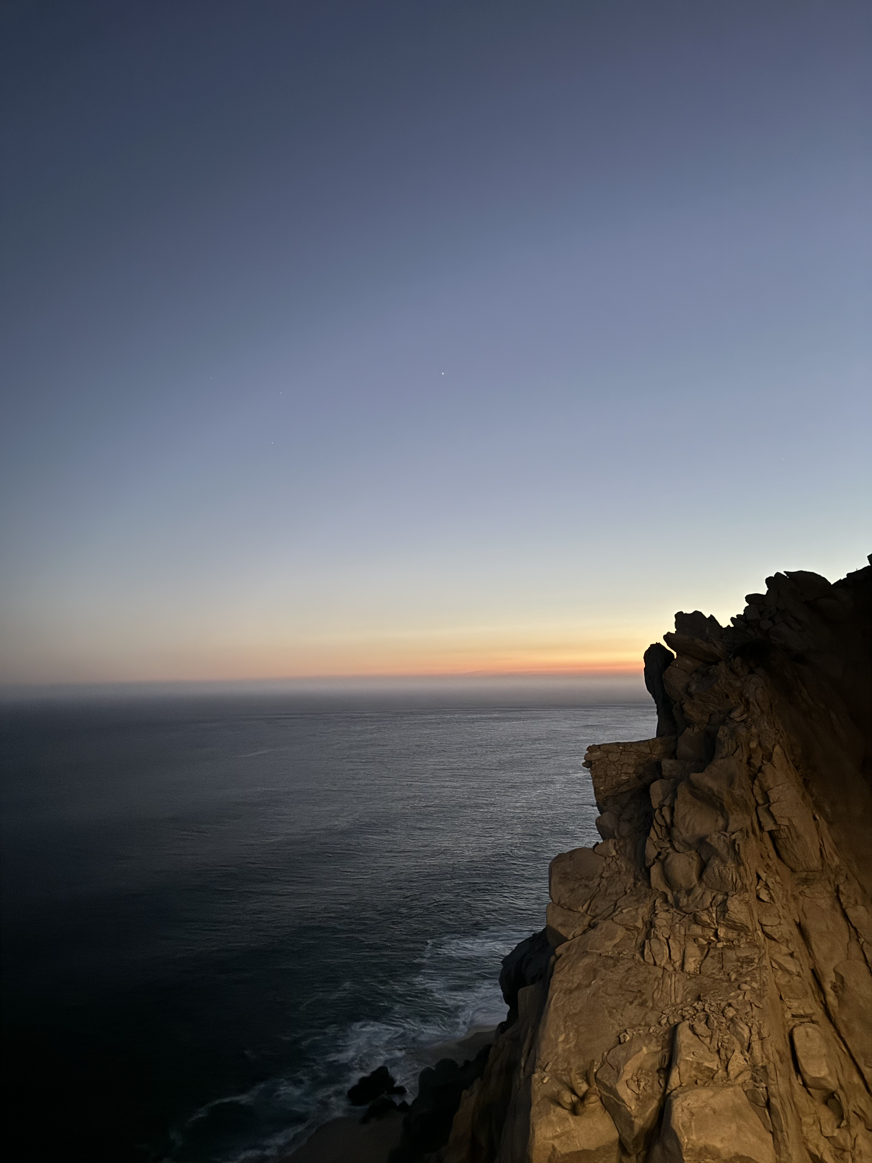 Sunset view over an ocean with rugged cliffside in the foreground, illustrating natural beauty and tranquility. No people or text present