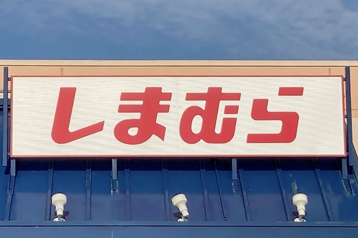 Storefront with Japanese text sign that reads “Shimamura” above an entrance, under a blue sky