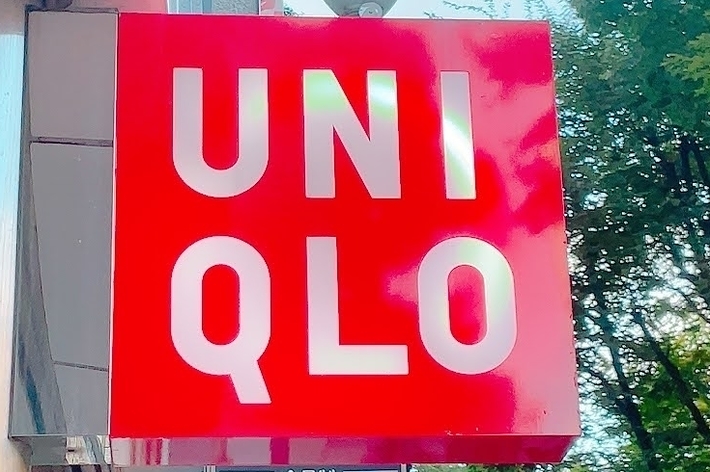 Red UNIQLO store sign mounted on a building, with trees seen in the background