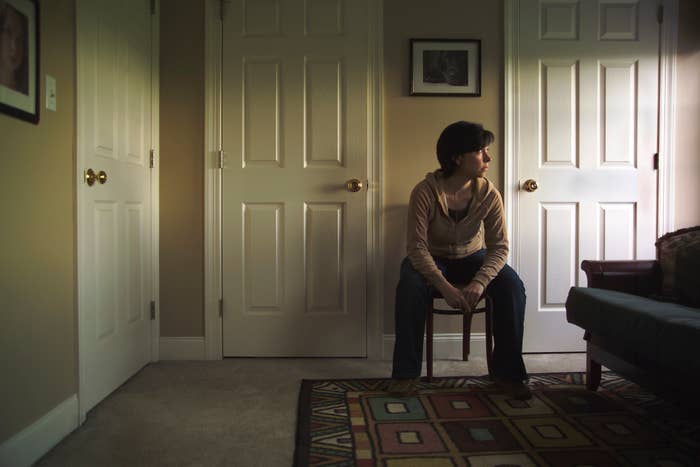 A person sitting on a chair in a room facing sideways, with three closed doors and a rug on the floor