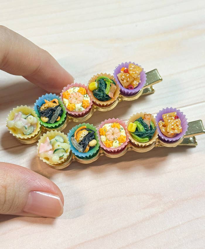 手作りのミニチュア食品がデザインされたヘアクリップを持っている手の画像。