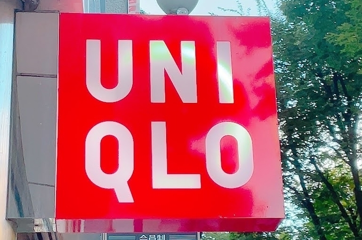A red Uniqlo sign is mounted on a building, with trees visible in the background. A smaller sign below has Japanese text