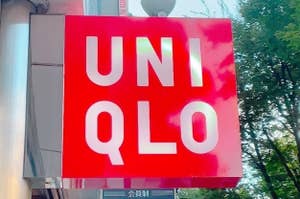 A red and white UNIQLO store sign is hanging on an exterior wall with trees visible in the background
