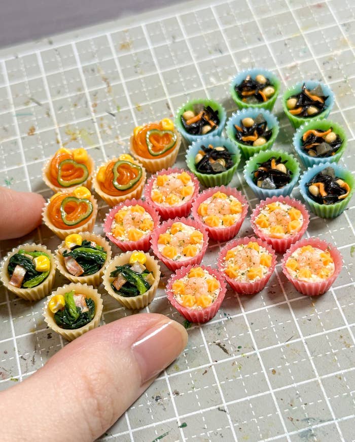 ミニチュア食品の写真。指と比べて小さな、色とりどりのカップに入ったサラダや料理が並べられている。