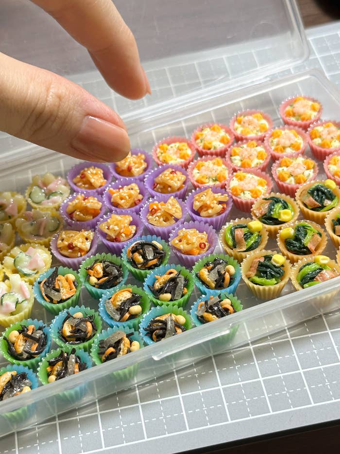 人の指が、多種多様な一口サイズのお菓子が並んだ透明なケースから一つを取ろうとしている。