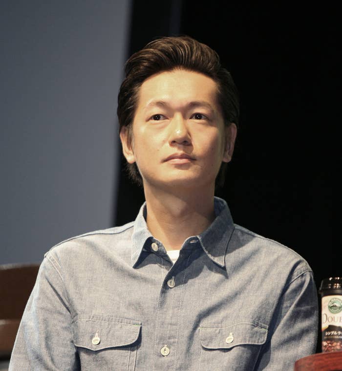 男性がカジュアルなデニムシャツを着て壇上に座っている。