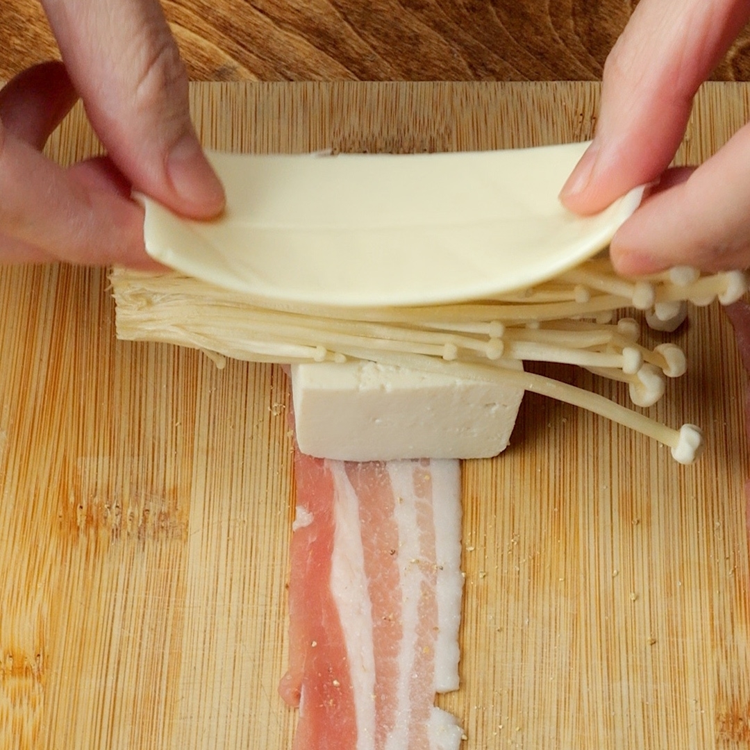 手で豚バラに豆腐、えのき、スライスチーズを巻いている様子。